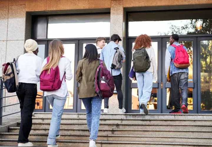 Gruppo di studenti con zaini sale le scale verso l'edificio scolastico, forse per affrontare una grave punizione scolastica.