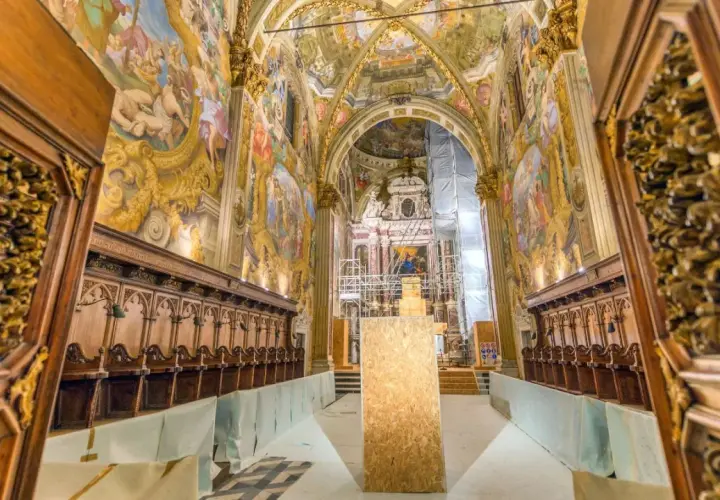 Interno della Certosa di Pavia, con affreschi dorati, stalli lignei e un'impalcatura. Cosa vedere in questo capolavoro.