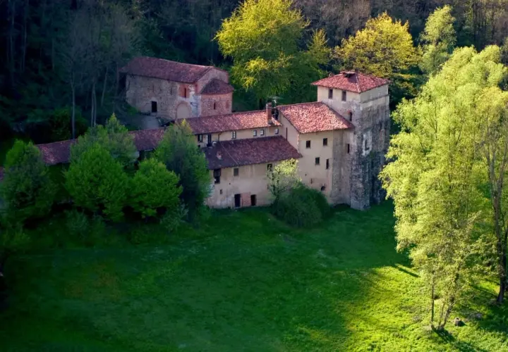 Antico monastero di Torba immerso nel verde, con tetti rossi e torri in pietra, circondato da alberi rigogliosi.