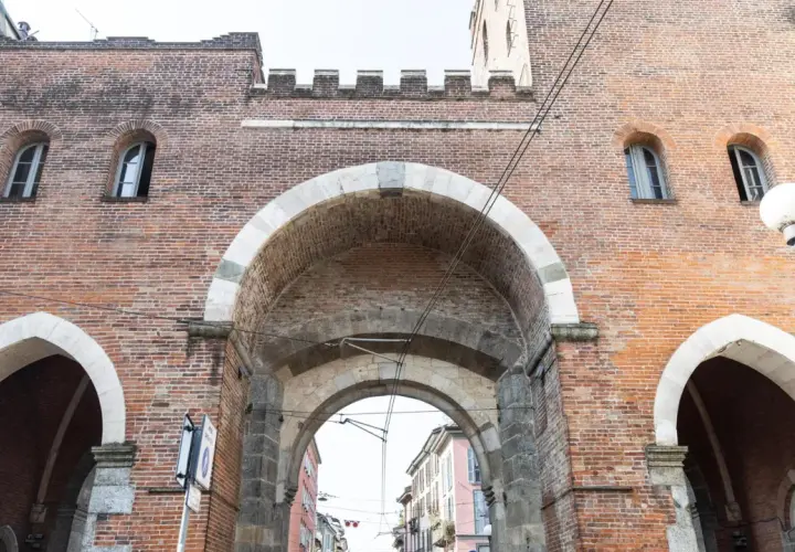 La Porta Ticinese, con i suoi archi in pietra e mattoni rossi, accoglie la vista di una strada milanese.