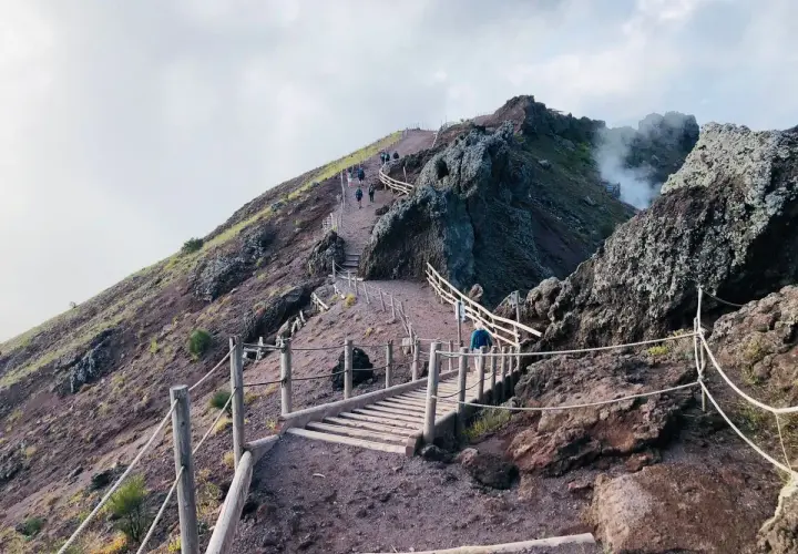 Sentiero sul gran cono Vesuvio, con persone che salgono verso il cratere fumante.
