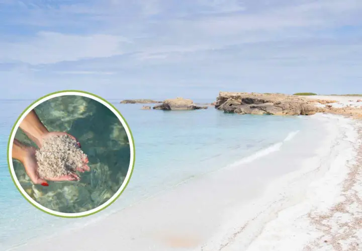Mani raccolgono sabbia bianca e fine su una spiaggia di vetro in Sardegna, con acque cristalline e rocce sullo sfondo.