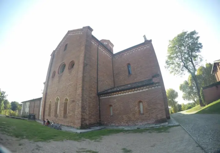 L'imponente facciata in mattoni dell'abbazia di Morimondo si staglia contro il cielo. Alcune persone e biciclette riposano sull'erba.