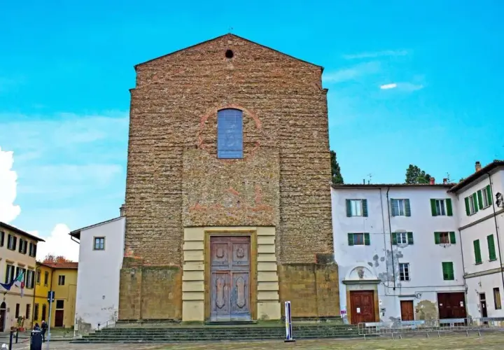 La facciata in pietra grezza di Santa Maria del Carmine domina la piazza, con un grande portale in legno e un rosone blu.