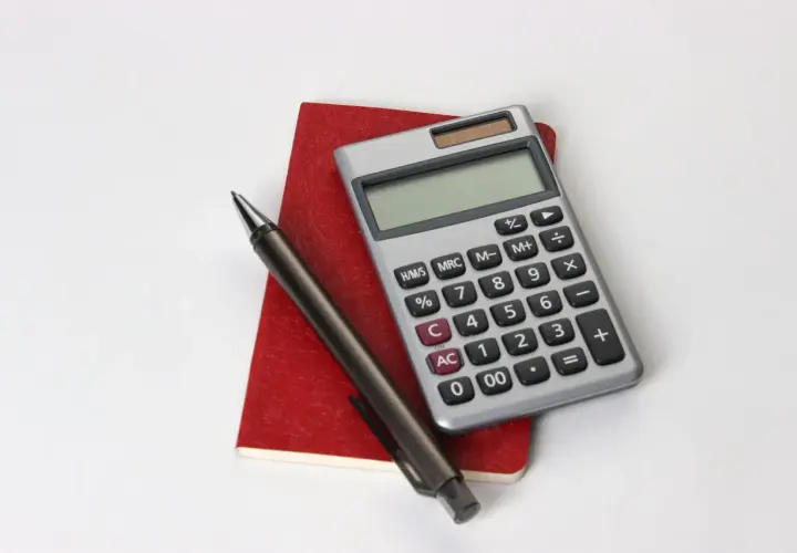Calcolatrice, penna e taccuino rosso, utili per consultare la tabella importi pensione insegnanti.