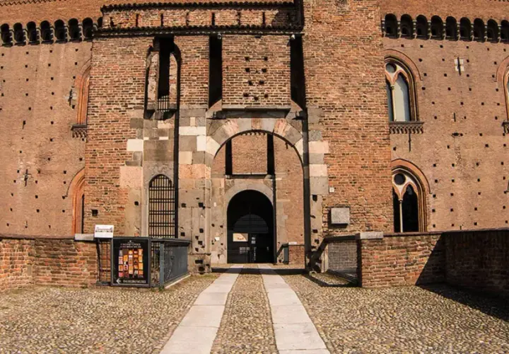 Ingresso principale del castello visconteo di Pavia, con mura in mattoni rossi, finestre ogivali e un ampio portone ad arco.