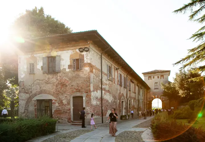 Passeggiata serale all'abbazia di Chiaravalle, con edifici storici in mattoni e un arco d'ingresso illuminato dal sole.
