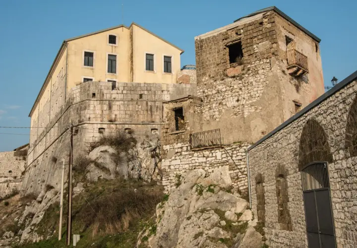 Antiche mura e un edificio giallo a Montesarchio, Benevento, si stagliano contro il cielo azzurro.