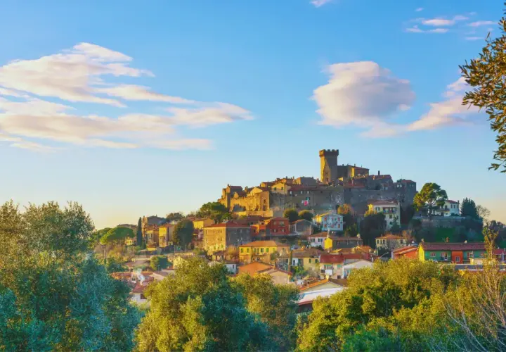 Un caparbio paese arroccato su una collina, con un castello imponente e case colorate, illuminato dalla luce dorata del tramonto.