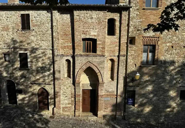 Antica facciata in pietra e mattoni a Macerata Feltria, con un portale ad arco e finestre storiche.
