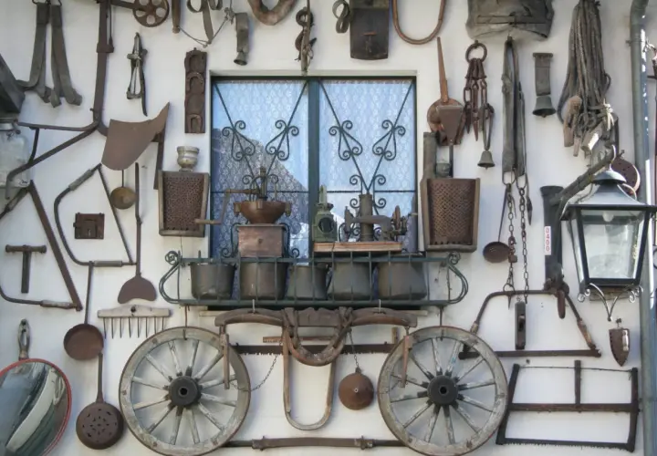 Vecchi attrezzi agricoli e oggetti d'epoca adornano un muro a Bienno, Brescia, creando un'installazione artistica che racconta storie di un tempo passato.