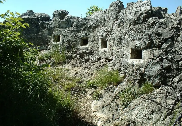 Antiche trincee della Linea Cadorna scavate nella roccia, con feritoie che si affacciano su un paesaggio verdeggiante.