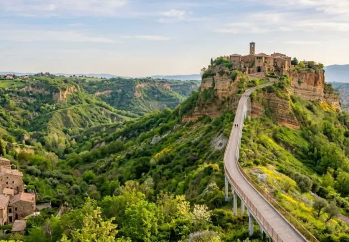 Ponte pedonale verso Civita di Bagnoregio, un borgo medievale arroccato su una rupe, circondato da verdi calanchi.
