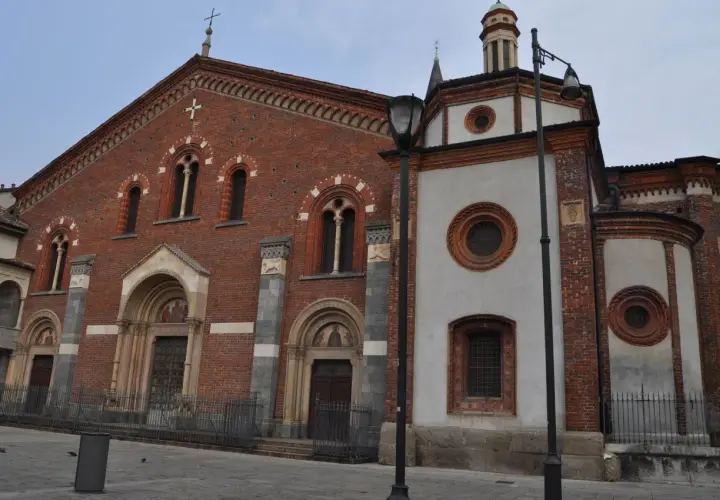 Facciata in mattoni rossi e parte in intonaco bianco della Basilica di Sant'Eustorgio a Milano, con portali decorati e finestre ad arco.