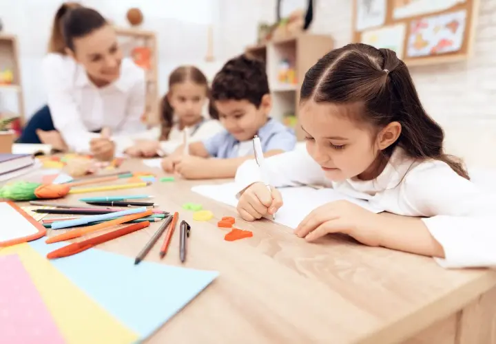 Bambini concentrati scrivono, un'insegnante li osserva. Un'immagine che ispira per una domanda motivazionale TFA sostegno.