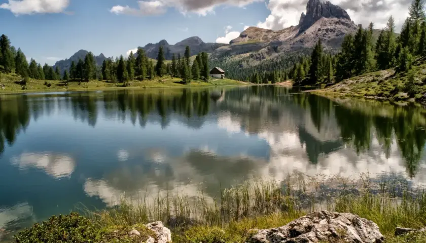 Lago alpino con riflessi di montagne e nuvole, un piccolo rifugio tra i pini. Uno dei paesi più belli del Cadore.