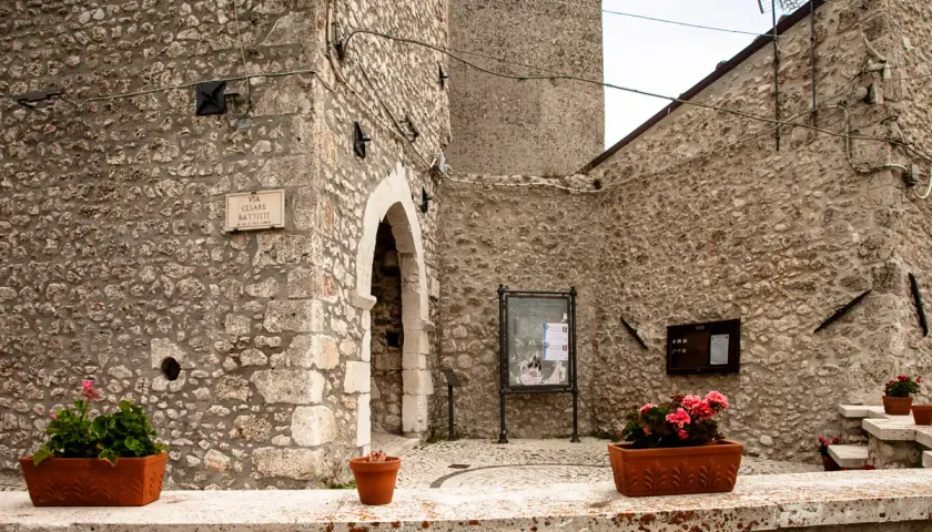 Un angolo suggestivo di Castel del Monte, Abruzzo, con muri in pietra grezza, un arco antico e vasi fioriti che aggiungono colore.