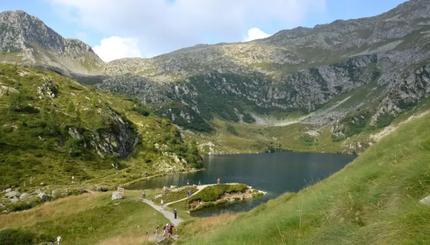 Sentiero panoramico per il giro dei 5 laghi a Madonna di Campiglio, con escursionisti che ammirano il lago alpino e le montagne circostanti.