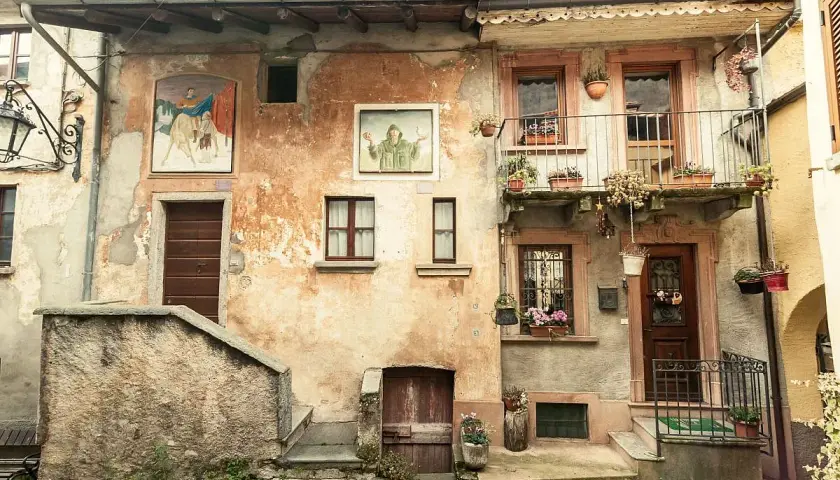 Antica facciata con affreschi e balcone fiorito. Un invito a scoprire cosa vedere ad Arcumeggia, tra arte e storia.