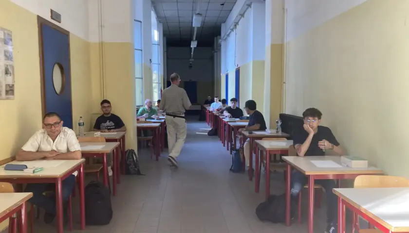 Studenti seduti ai banchi in un'aula scolastica, concentrati sull'esame di quinta elementare. Un insegnante cammina tra i banchi.