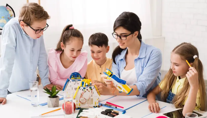 Bambini e insegnante costruiscono robot, un'attività che illustra il significato di itp scuola: apprendimento pratico e innovazione.