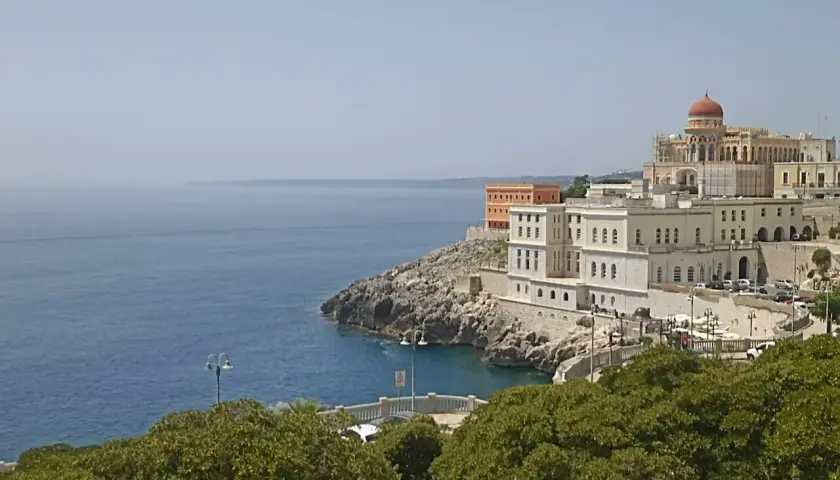 Vista sul mare e sul complesso dell'istituto alberghiero Santa Cesarea Terme, con edifici bianchi e una cupola rossa.