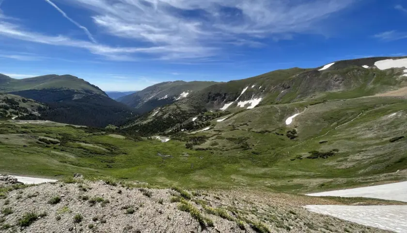 Vasta valle alpina con prati verdi, macchie di neve e cielo azzurro. Un paesaggio mozzafiato che ricorda l'altitudine chiusa di Bolzano.