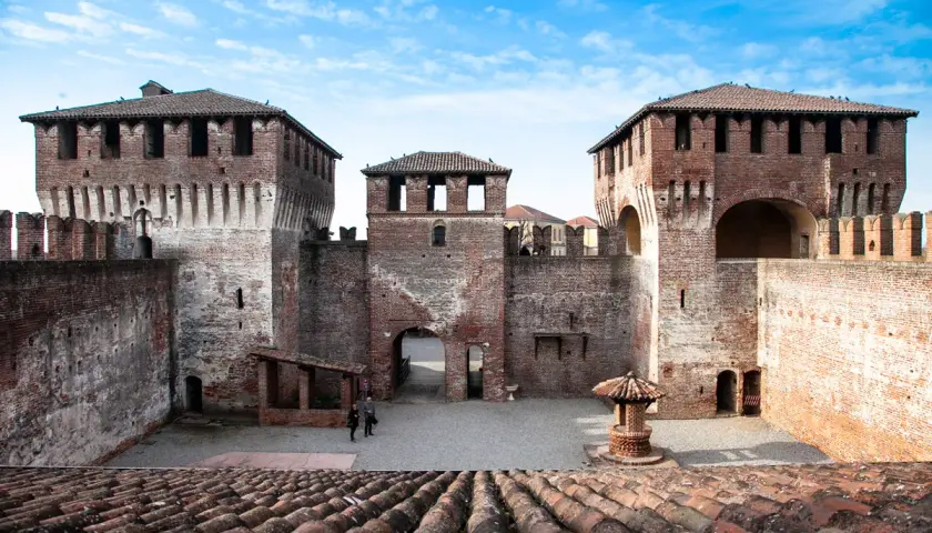 Il castello di Soncino, con le sue imponenti torri in mattoni rossi e le mura merlate, si staglia sotto un cielo azzurro e nuvoloso.