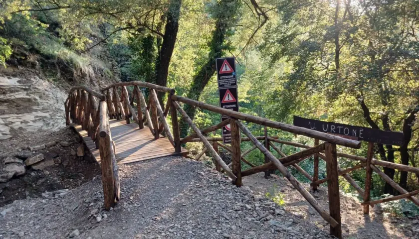 Ponte in legno rustico conduce verso le cascate di San Fele, immerso nel verde e illuminato dal sole.