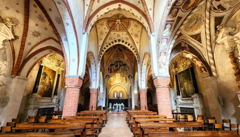 Interno dell'abbazia di Viboldone con volte affrescate, colonne in mattoni e panche di legno.