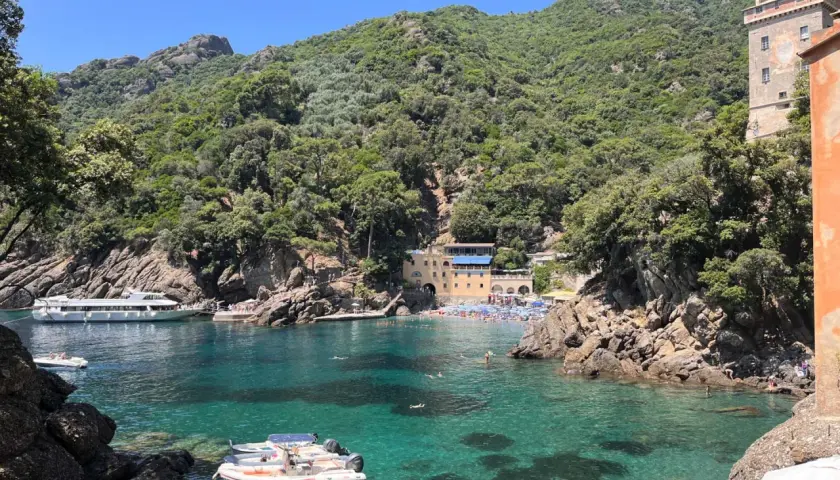 Baia di San Fruttuoso con acque cristalline, barche e persone che nuotano. Un luogo ideale per il trekking e il relax.