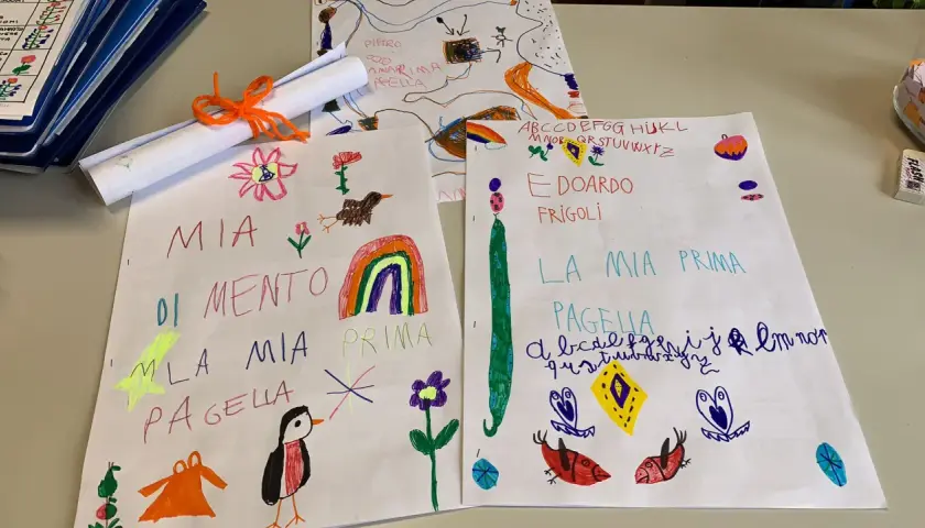 Disegni e scritte a mano, tra cui "Mia Pagella" e l'alfabeto, mostrano i voti elementari di bambini.