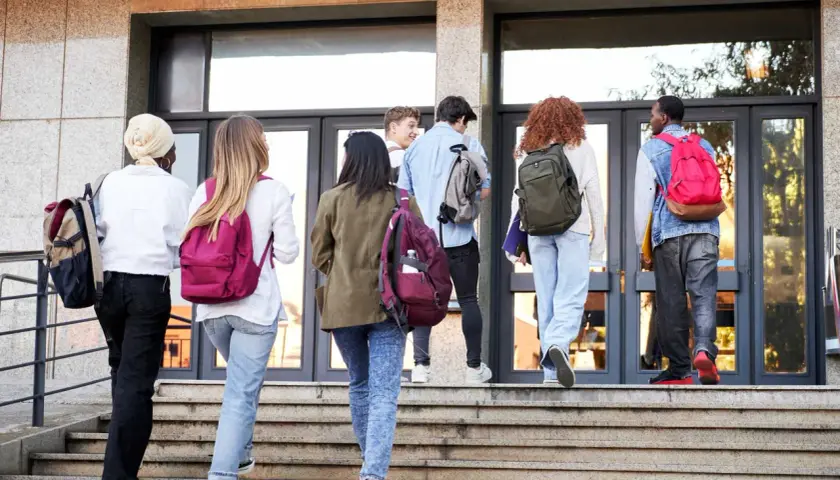 Gruppo di studenti con zaini sale le scale verso l'edificio scolastico, forse per affrontare una grave punizione scolastica.