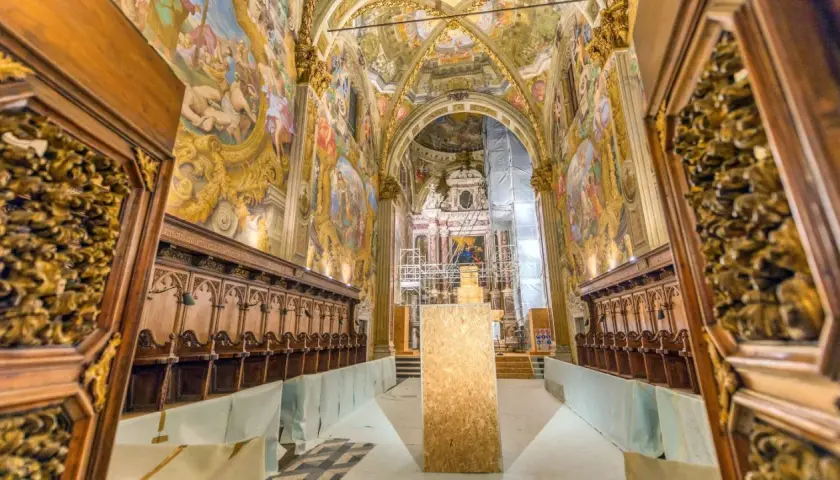 Interno della Certosa di Pavia, con affreschi dorati, stalli lignei e un'impalcatura. Cosa vedere in questo capolavoro.