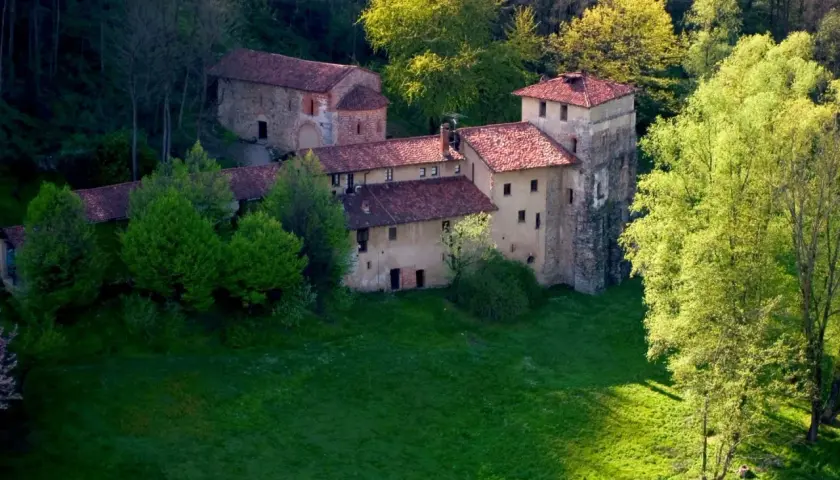 Antico monastero di Torba immerso nel verde, con tetti rossi e torri in pietra, circondato da alberi rigogliosi.