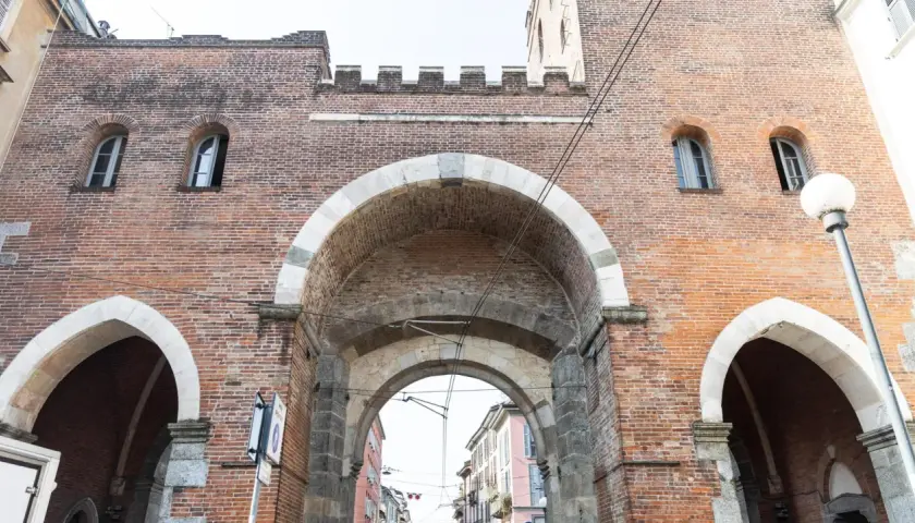 La Porta Ticinese, con i suoi archi in pietra e mattoni rossi, accoglie la vista di una strada milanese.