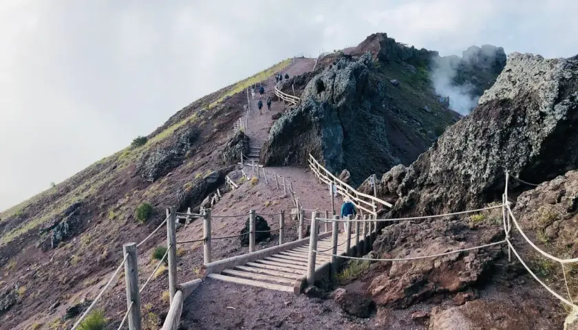 Sentiero sul gran cono Vesuvio, con persone che salgono verso il cratere fumante.