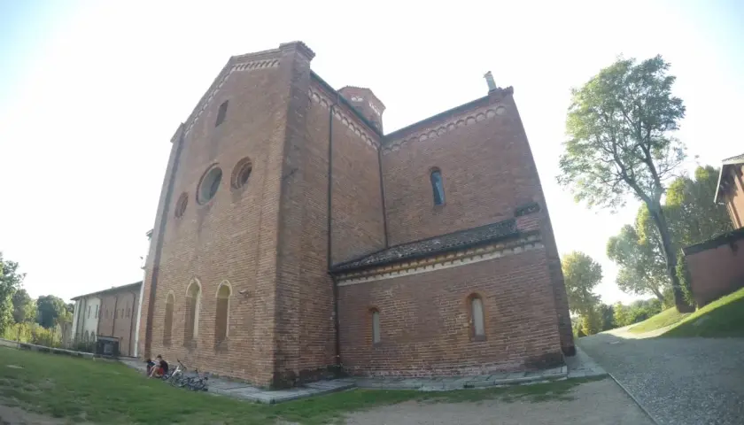 L'imponente facciata in mattoni dell'abbazia di Morimondo si staglia contro il cielo. Alcune persone e biciclette riposano sull'erba.