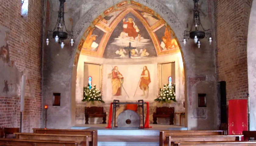Interno di una chiesa con affreschi antichi e panche di legno. L'altare presenta un dipinto di San Cristoforo, simbolo di protezione per i viaggiatori a San Cristoforo, Milano.