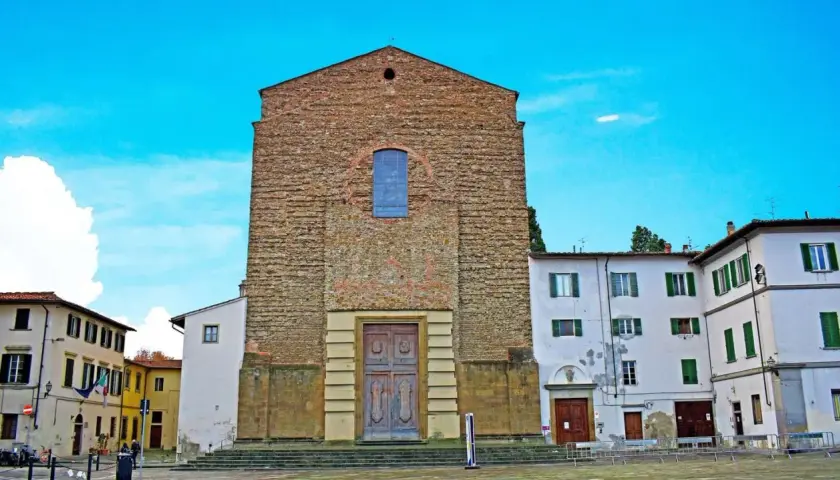 La facciata in pietra grezza di Santa Maria del Carmine domina la piazza, con un grande portale in legno e un rosone blu.