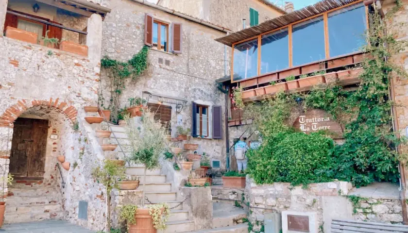 Un angolo incantevole tra i borghi vicino Capalbio, con scale di pietra, vasi di terracotta e la trattoria "La Torre" avvolta dal verde.