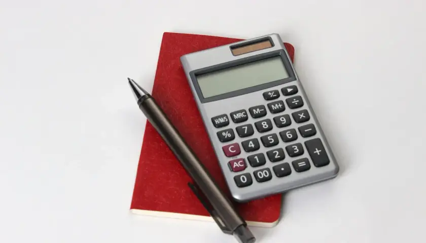 Calcolatrice, penna e taccuino rosso, utili per consultare la tabella importi pensione insegnanti.