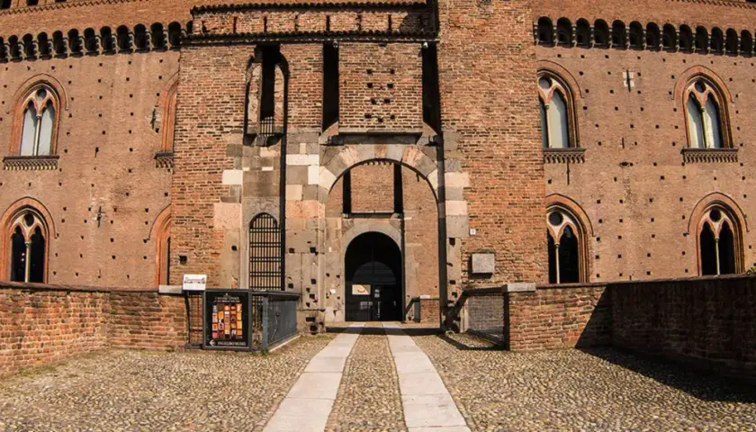 Ingresso principale del castello visconteo di Pavia, con mura in mattoni rossi, finestre ogivali e un ampio portone ad arco.
