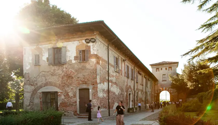 Passeggiata serale all'abbazia di Chiaravalle, con edifici storici in mattoni e un arco d'ingresso illuminato dal sole.