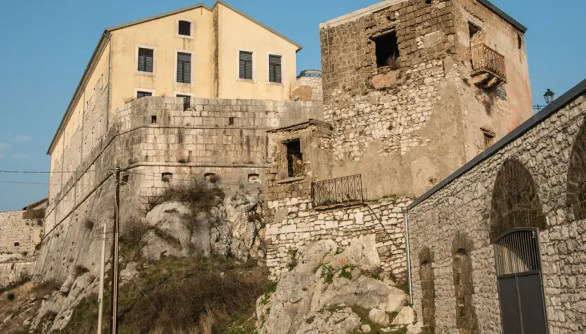 Antiche mura e un edificio giallo a Montesarchio, Benevento, si stagliano contro il cielo azzurro.