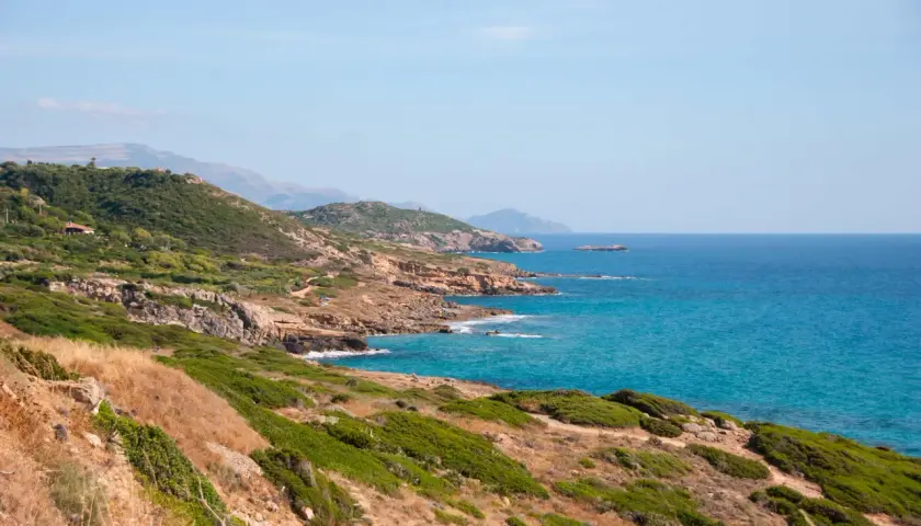 Costa selvaggia tra Alghero e Bosa, con macchia mediterranea, rocce dorate e mare turchese.