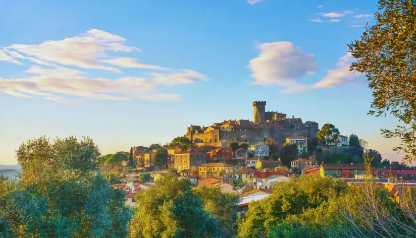 Un caparbio paese arroccato su una collina, con un castello imponente e case colorate, illuminato dalla luce dorata del tramonto.