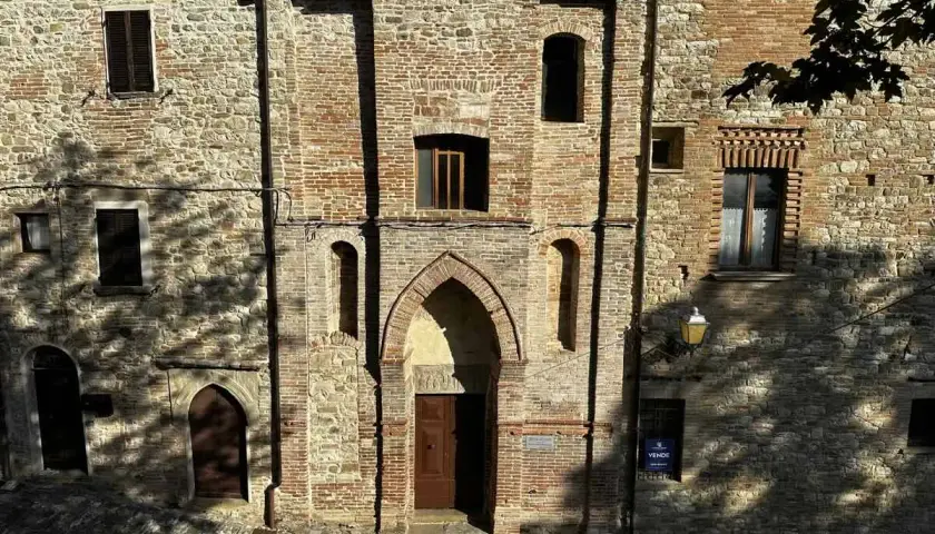 Antica facciata in pietra e mattoni a Macerata Feltria, con un portale ad arco e finestre storiche.