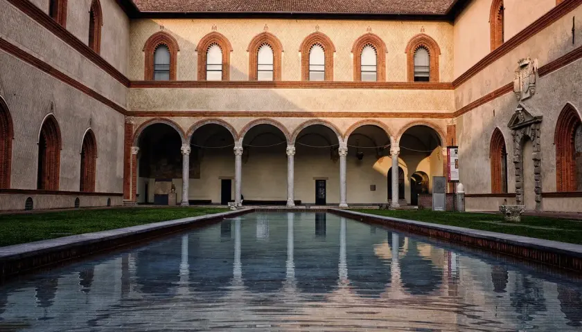 Cortile del Castello Sforzesco con piscina riflettente e portico ad archi.