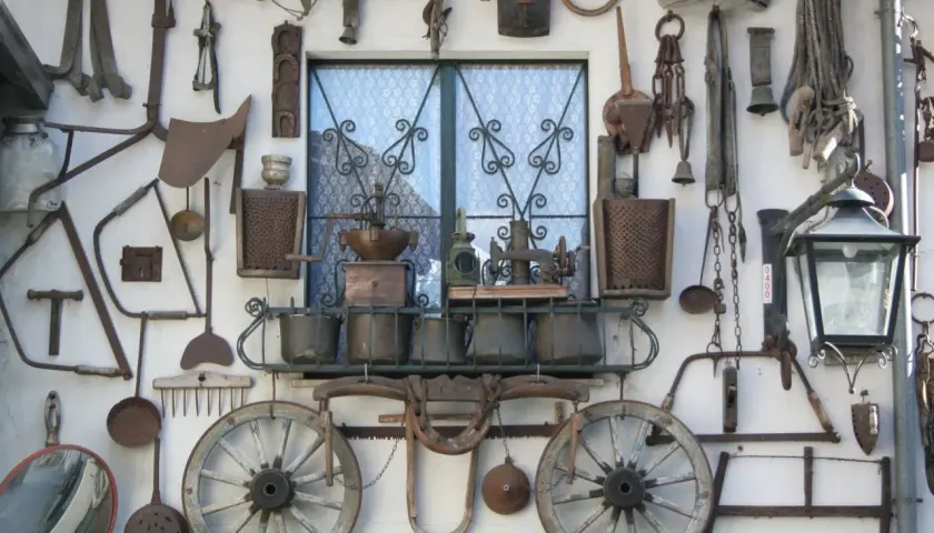 Vecchi attrezzi agricoli e oggetti d'epoca adornano un muro a Bienno, Brescia, creando un'installazione artistica che racconta storie di un tempo passato.